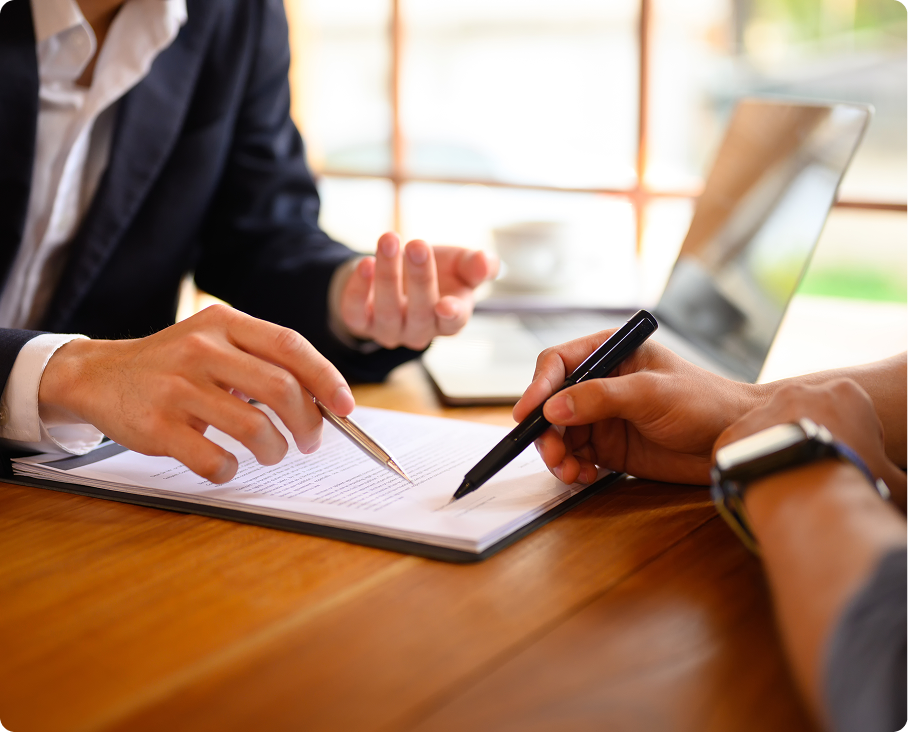 Two people reviewing and signing documents at a wooden table.